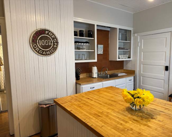 The image shows a modern kitchen with a wooden island, equipped with a sink and white cabinetry, featuring a decorative "Farm Fresh 100% Organic" sign on the wall.