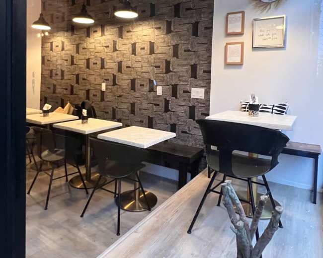 The image shows a modern café interior with patterned wallpaper, wooden tables, and black chairs, illuminated by hanging pendant lights.