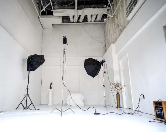 A photography studio features two softbox lights, a backdrop stand, and decorative elements against white walls.
