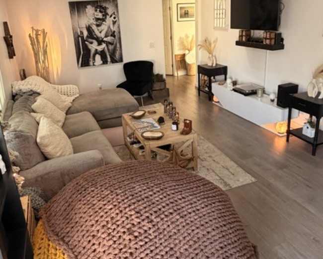 A cozy living room features a large sectional sofa, a coffee table with various decorative items, and a wall-mounted television, with artwork and plants adding to the ambiance.