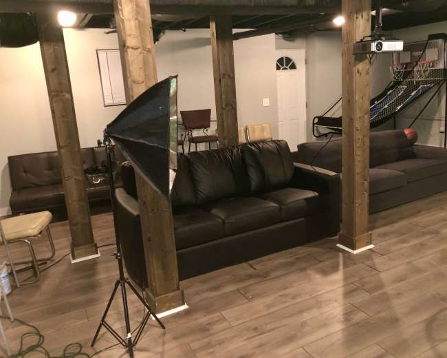 A spacious basement living area with two couches, wooden support beams, and a projector setup.