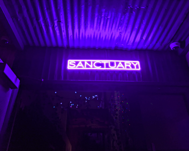 A brightly lit purple neon sign displays the word "SANCTUARY" above an entrance.