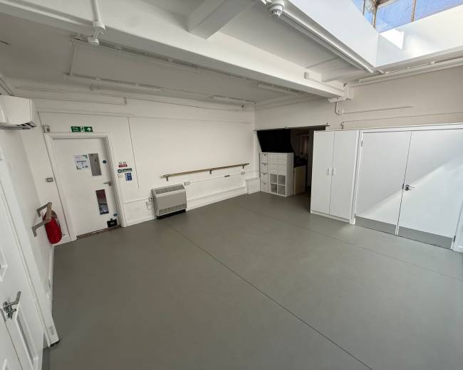 The image shows a spacious, minimalist studio with white walls, a skylight, and a light gray floor.