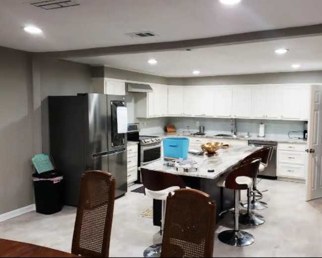 The image shows a modern kitchen with stainless steel appliances, white cabinetry, and a central island with bar stools.