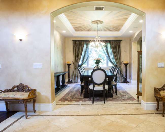 An interior space with a dining area featuring a black table and elegant chairs, framed by decorative walls and a chandelier.