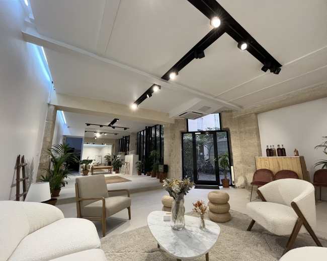 The image shows a modern, minimalist interior space with light-colored walls, natural materials, and comfortable seating arrangements.