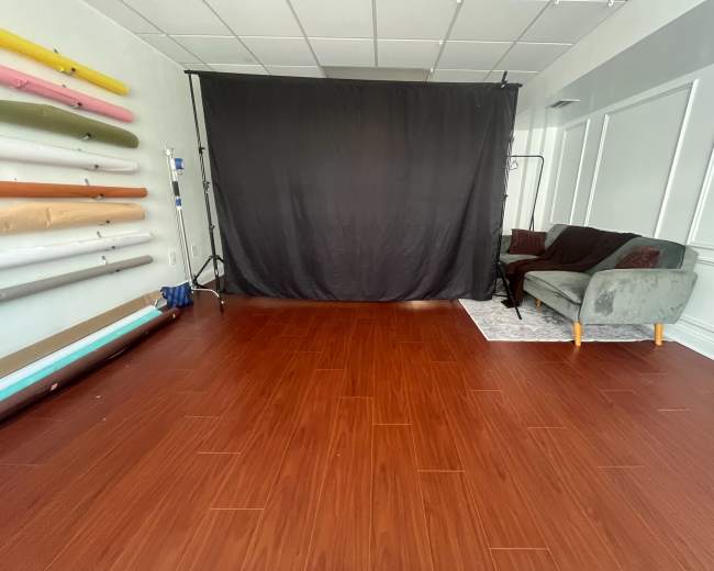 The image shows a spacious room with a dark backdrop, a gray sofa, and colorful rolls of backdrop paper arranged along one wall.