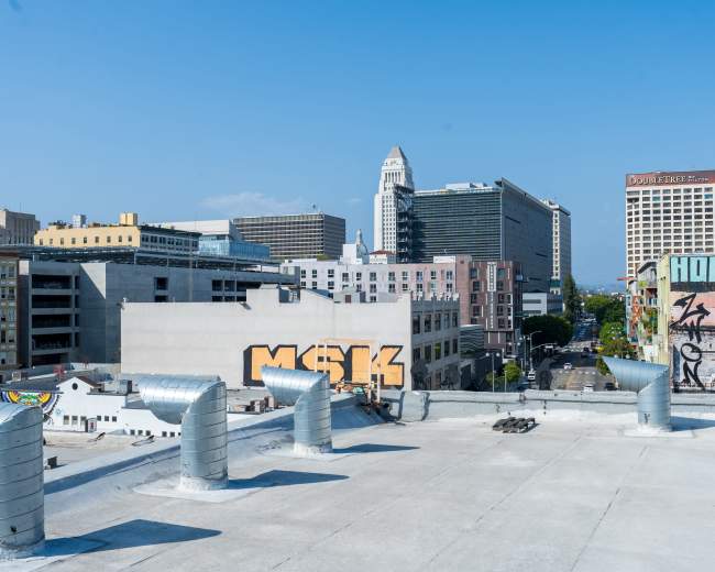 The image shows a rooftop view of a cityscape with several buildings, including skyscrapers and graffiti on the walls.