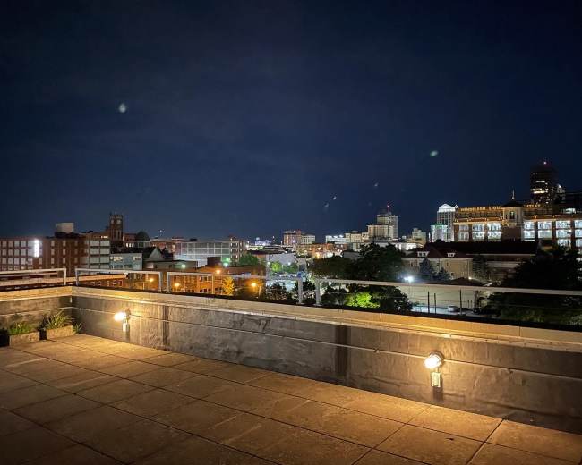 A rooftop terrace with a city skyline illuminated at night.