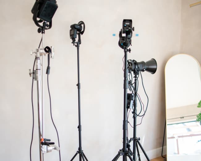 The image shows three photography light stands positioned near a wall with a mirror and wooden flooring.