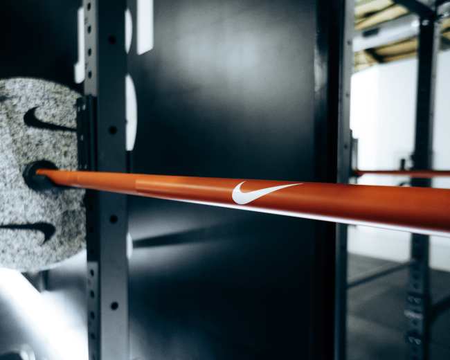 A close-up view of a barbell with a Nike-branded weight plate on a rack in a gym.