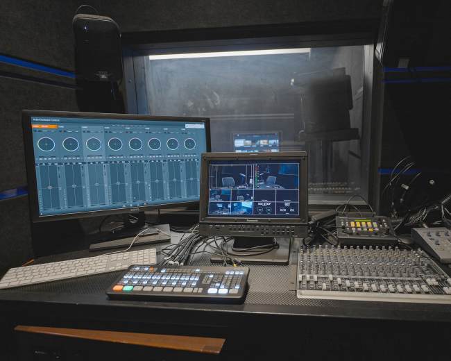 This image shows a video production control room with multiple monitors, a mixing console, and various cables.