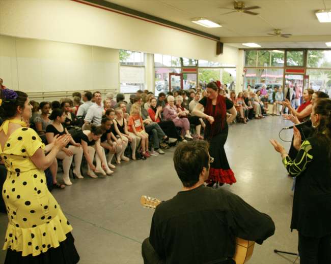 A group of dancers perform in front of an audience seated in a dance studio.