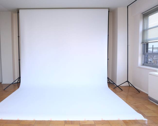 A large white backdrop set up in a room with wooden flooring and a window.