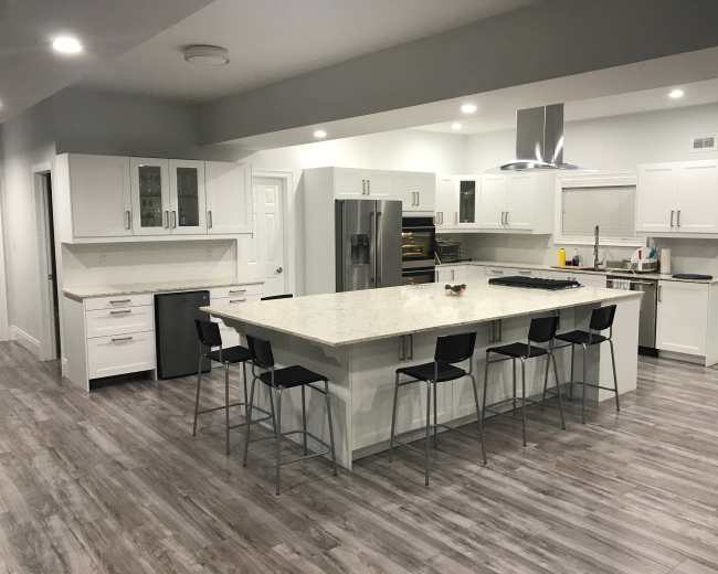 The image shows a modern kitchen featuring a large island with bar stools, white cabinetry, and stainless steel appliances.