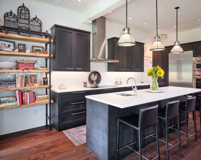 A modern kitchen features black cabinetry, a large white island with seating, and a vase of sunflowers on the counter, complemented by open shelving and stainless steel appliances.