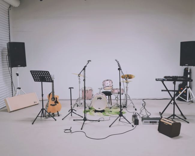 A music setup is arranged in a studio, featuring a drum kit, electric and acoustic guitars, microphones, and speakers.