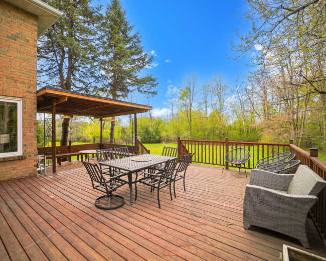 A wooden deck with a table and chairs overlooks a green landscape under a blue sky.