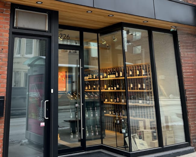 The entrance of a wine and food shop features large glass doors and a sign that reads "FINE ARTISANAL WINES & FOOD" above the doorway.