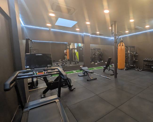 The image depicts a modern gym with various workout equipment, including a treadmill, weightlifting area, and a boxing bag, all arranged on rubber flooring.