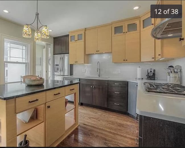 The image shows a modern kitchen featuring an island with storage, light wood cabinets, and stainless steel appliances.