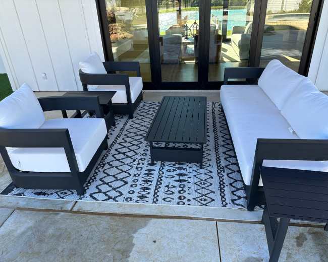 A seating area features two armchairs and a sofa arranged around a coffee table on a patterned rug, with a view of a pool in the background.