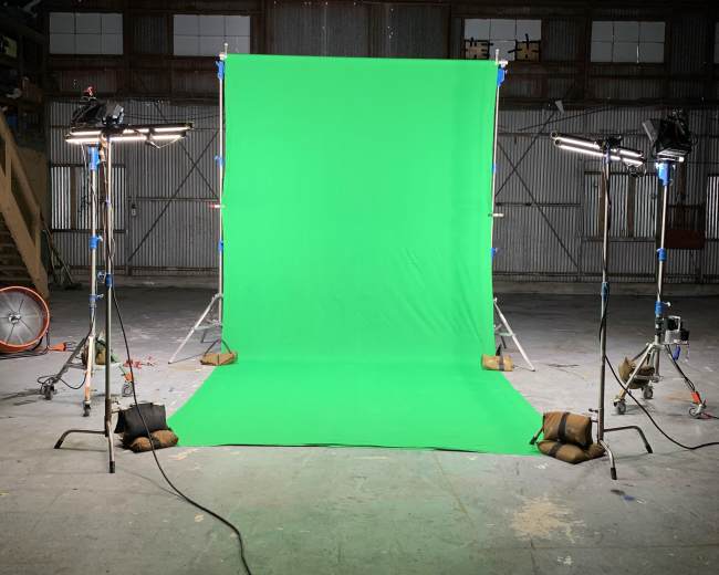 A green backdrop set up in an industrial space, illuminated by two lights on tripods.