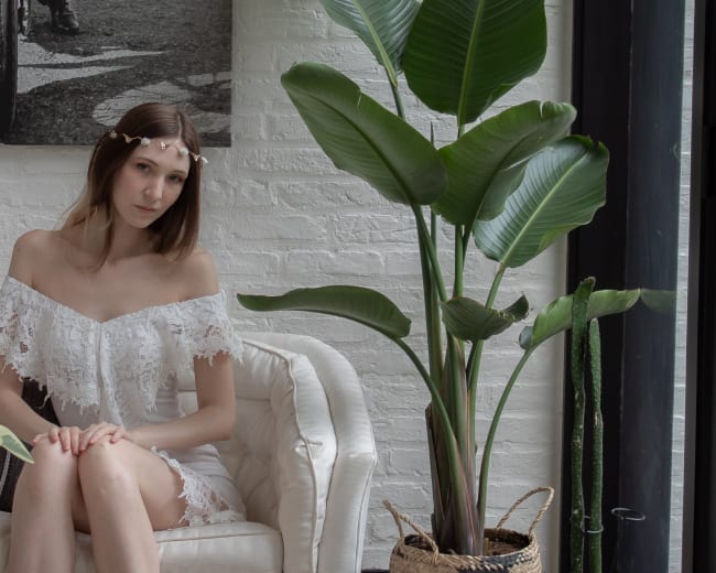 A woman sits on a white chair next to a large leafy plant in a bright, modern interior space.