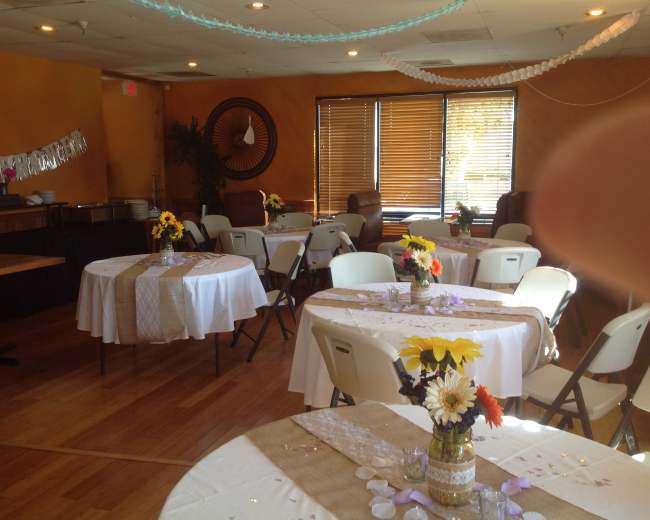 A banquet hall set with several round tables adorned with white tablecloths, centerpieces of flowers, and decorative details.