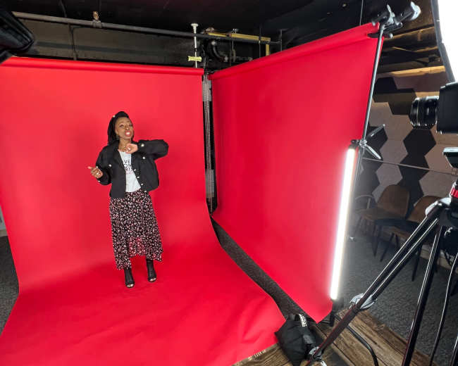 A person stands in front of a vibrant red backdrop in a photography studio, with studio lights and a camera set up nearby.