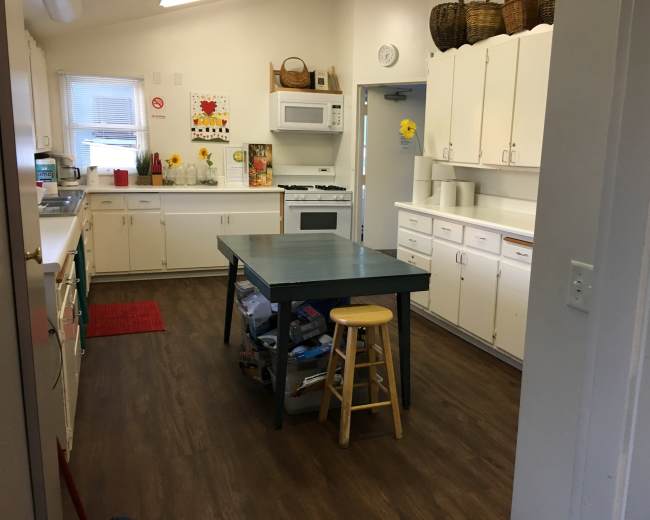 A kitchen featuring white cabinets, a central green table with a stool, and various appliances.