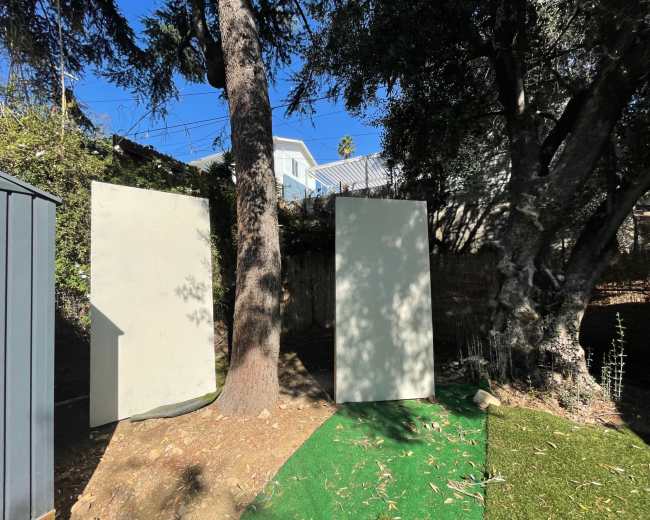 Two large, blank panels stand upright in a backyard surrounded by trees and grass.