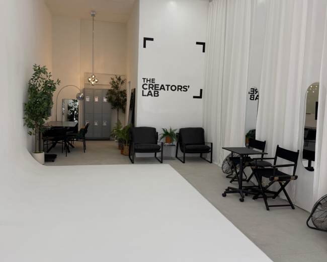 The image shows a minimalist studio space named "The Creators' Lab," featuring white walls, a white floor, and seating areas with plants and mirrors.