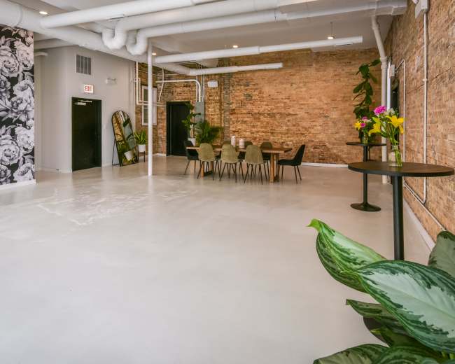 A spacious, modern interior with exposed brick walls, a large table set for dining, and decorative plants.