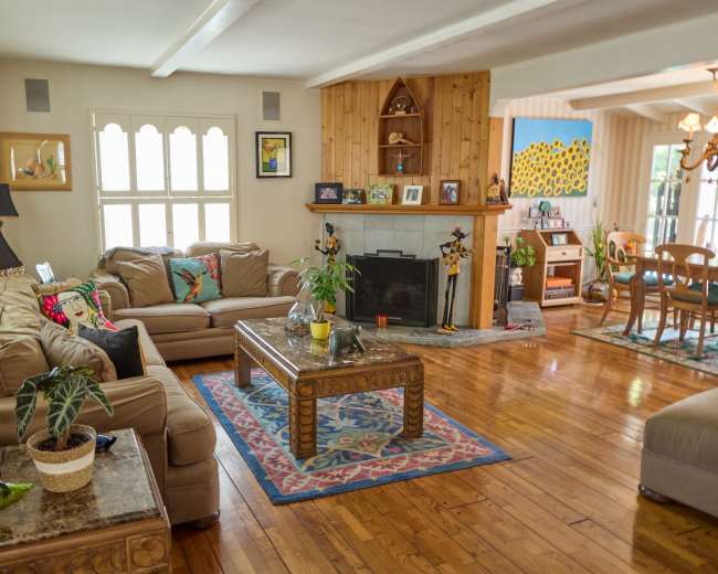The image depicts a living room with a comfortable seating area, a coffee table, a fireplace, and sunlight illuminating the wooden floors.