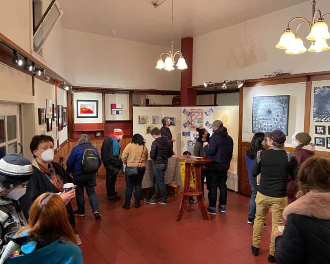 A group of people gathers in an art gallery, viewing various artworks displayed on the walls.