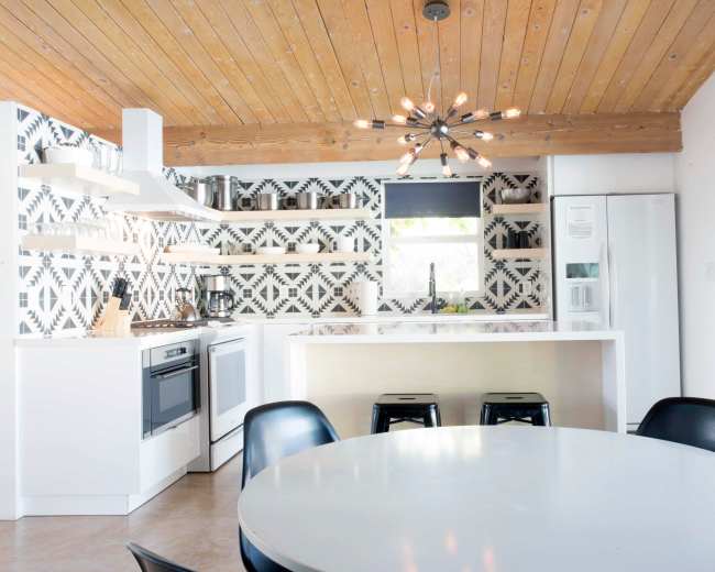 A modern kitchen features a wooden ceiling, geometric patterned walls, and a circular dining table with black chairs.