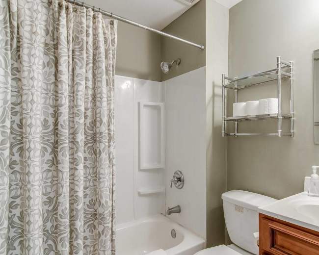 A bathroom features a bathtub with a shower, a sink with a wooden cabinet, and a mirror, all set against a green wall.