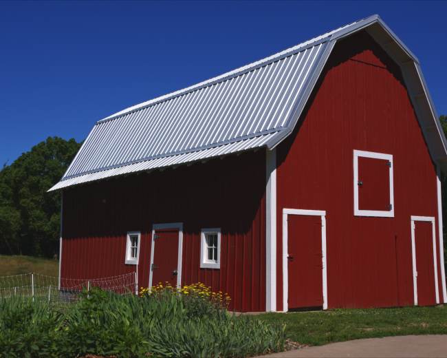 A red barn with a white roof and trim sits in a grassy field surrounded by trees.