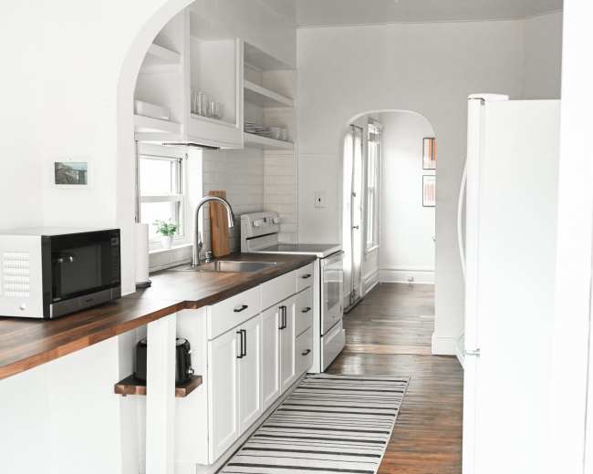 The image shows a modern kitchen with a wooden countertop, white cabinets, and a striped rug on the floor.