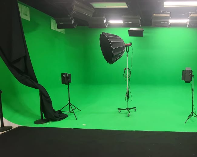 The image shows a green screen studio equipped with one large softbox light and two smaller lights on stands.