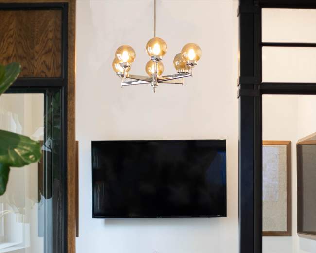 A modern meeting room features a round table with two chairs, a large wall-mounted TV, and a stylish light fixture above.