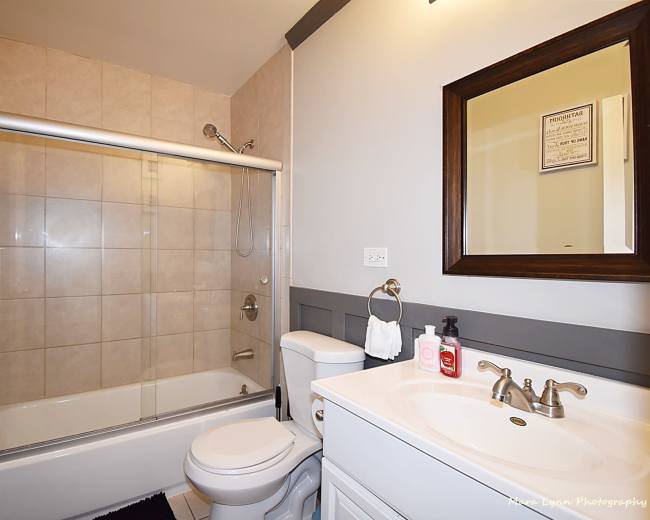 The image shows a bathroom with a bathtub-shower combination, a toilet, and a vanity with a mirror.