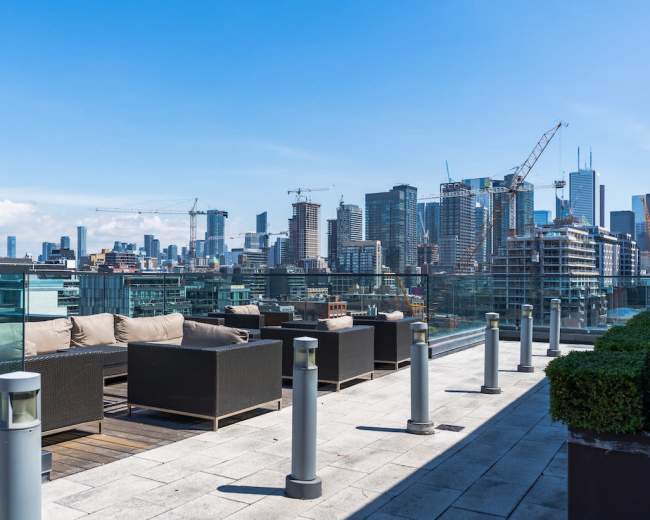 A rooftop terrace features seating and a panoramic view of a city skyline under a clear blue sky.