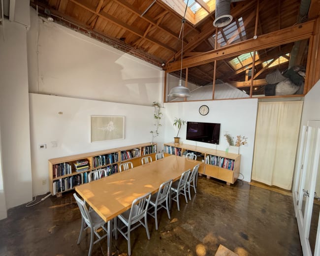 The image shows a spacious meeting room with a long wooden table, surrounded by chairs, and shelves filled with books along one wall.