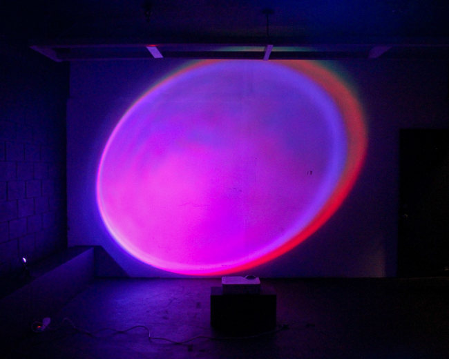 A colorful light projection illuminates a wall in a dimly lit room.
