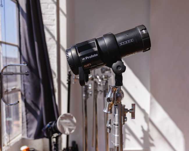 A studio light mounted on a stand is positioned near a window with natural light streaming in.