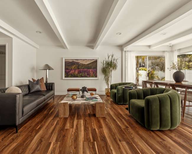 The living room features a black leather sofa, two green chairs, a wooden coffee table, and a large artwork on the wall.