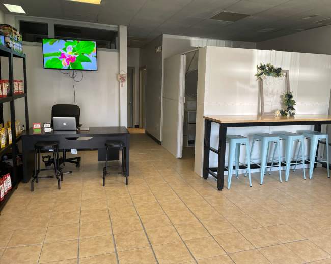 A spacious interior of a commercial space featuring a reception area with a desk and a TV, alongside a dining area with a long table and stools.