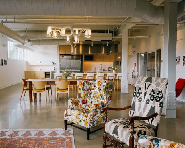 The image shows a modern kitchen and dining area with a long table, decorative chairs, and overhead lighting.